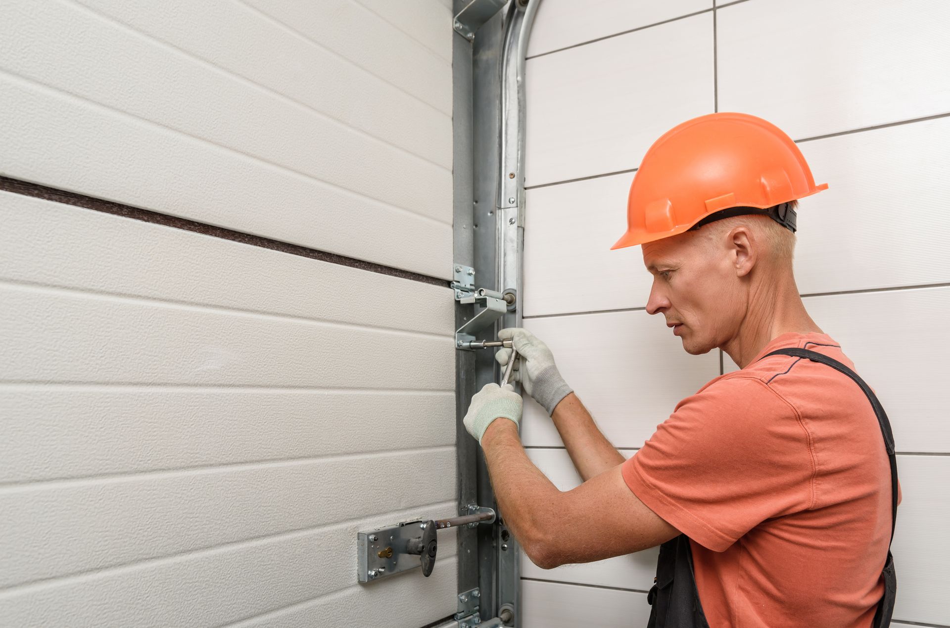 A male worker installs lift gates on a white garage’s door.