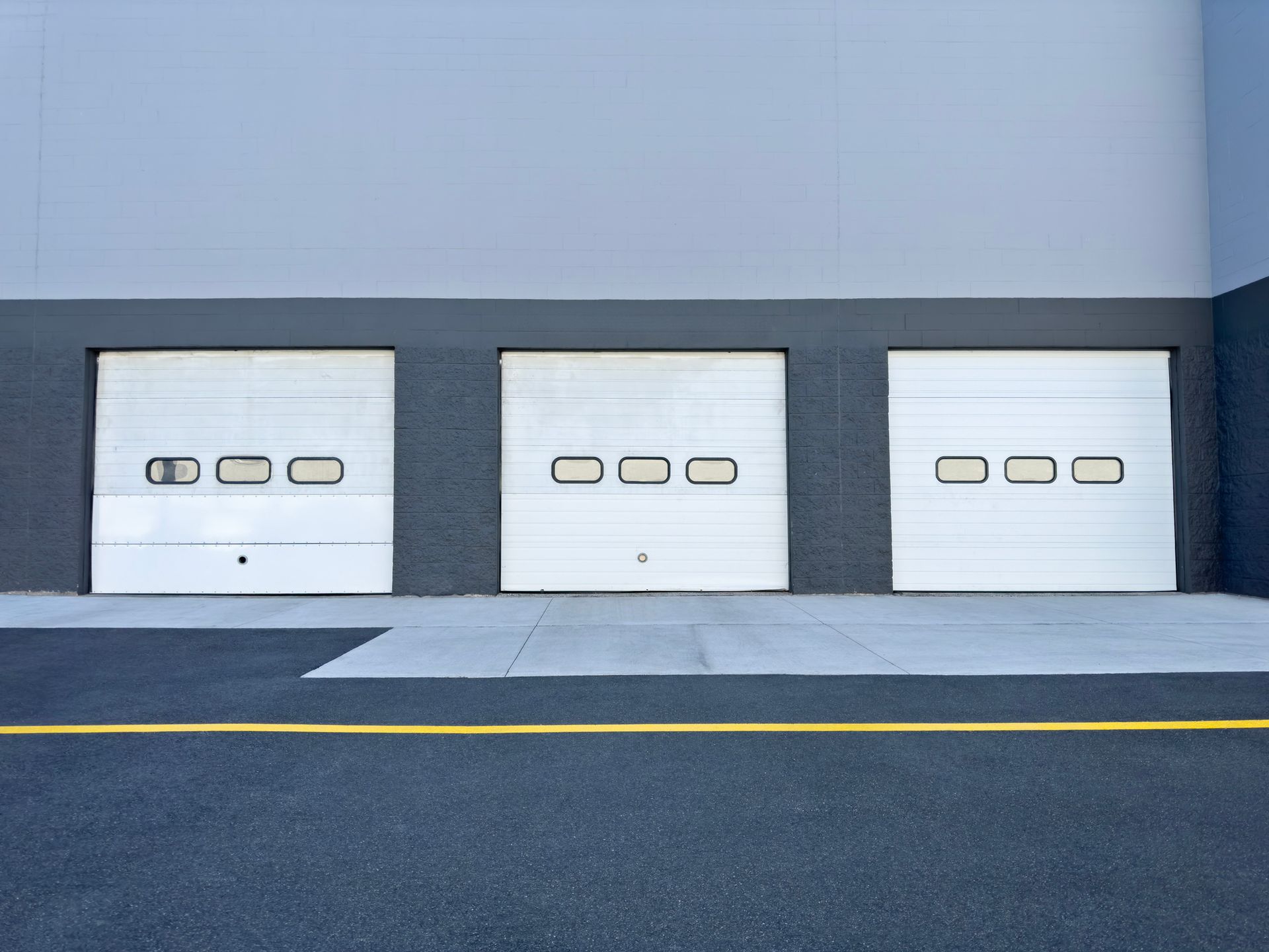 Three white garage doors on a gray building, set in front of asphalt pavement.