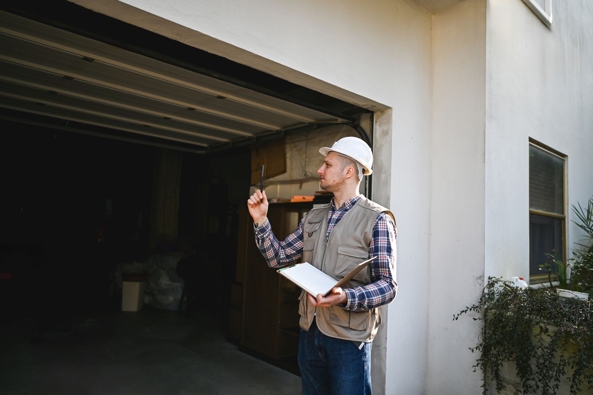 A person in a hard hat inspects a garage door with a tablet and pen.
