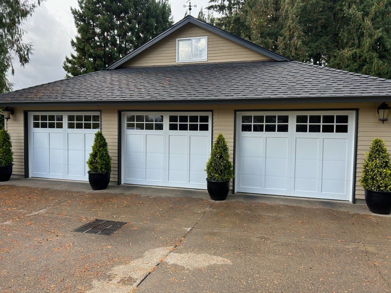 A garage with three white garage doors and potted plants in front of it
