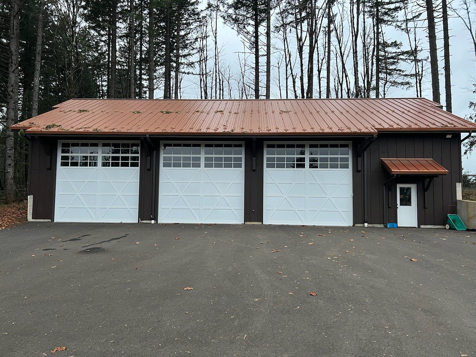 A garage with three white garage doors and a brown roof