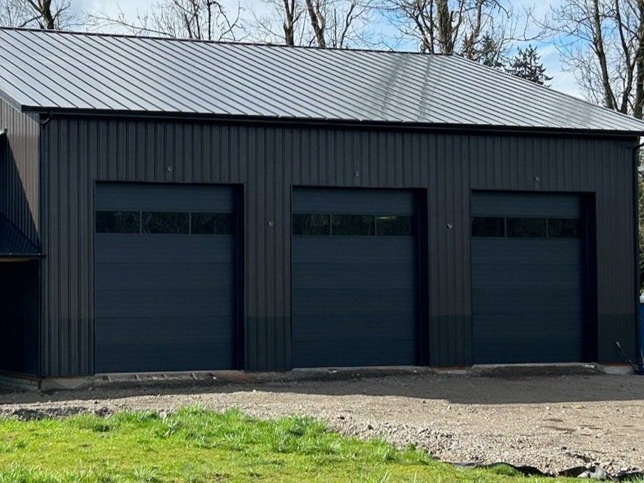 A black garage with three garage doors and a black roof.