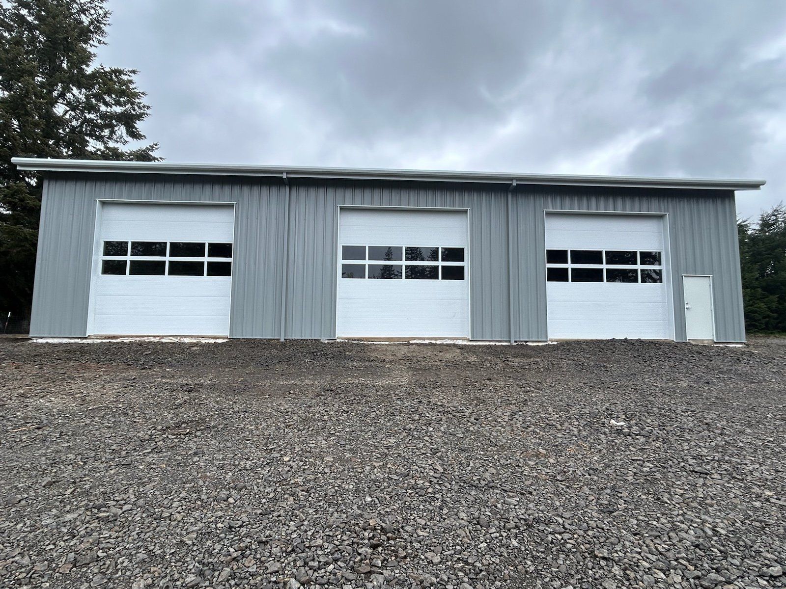 A garage with three white garage doors on a gravel road