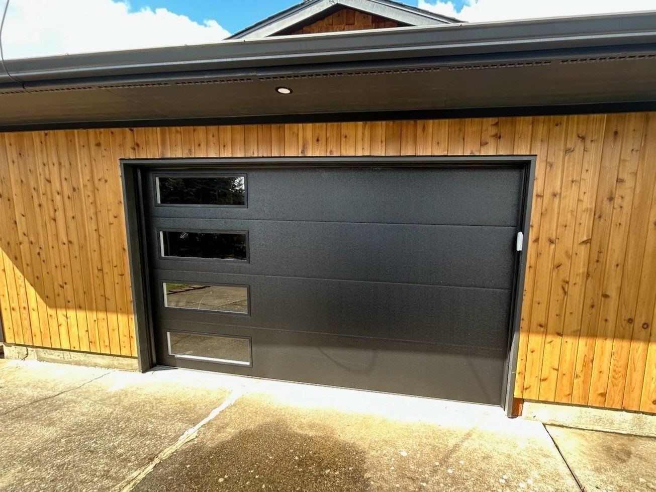 A black garage door is sitting on the side of a wooden house.