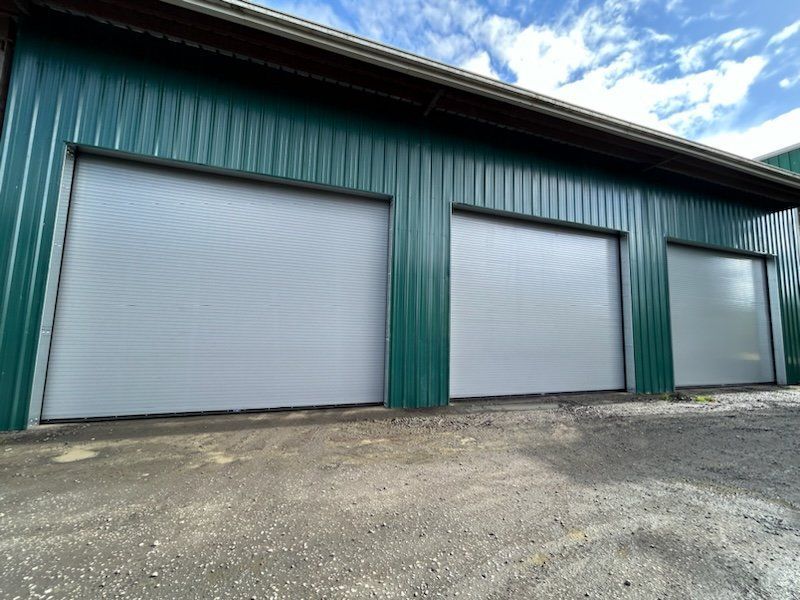 A green building with three white garage doors.