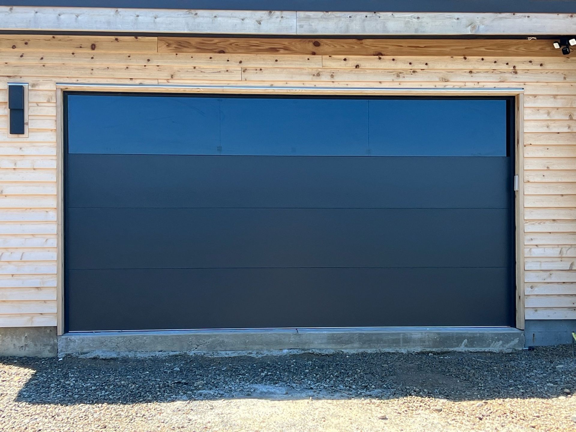 A black garage door is sitting in front of a wooden house.