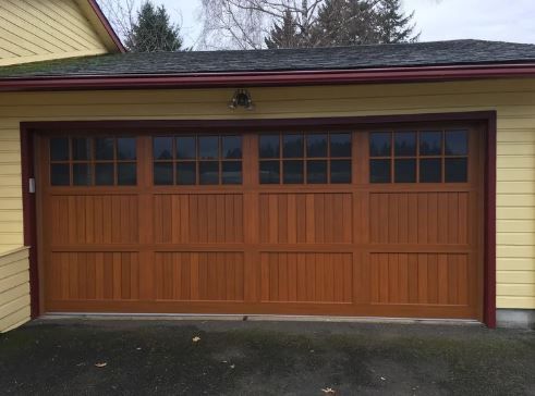 Brown wooden garage door with windows, on a yellow house.
