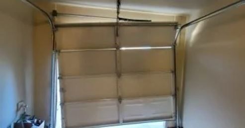 A partially open, white garage door is crooked in its frame. The setting is indoors, with beige walls.