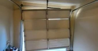 A partially open, white garage door is crooked in its frame. The setting is indoors, with beige walls.