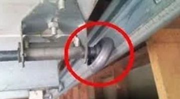 Close-up of a garage door track, a roller is broken and dislodged within the track, marked by a red circle.