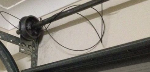 Garage door mechanism with a broken cable. The cable is wrapped around a rod and has come loose.
