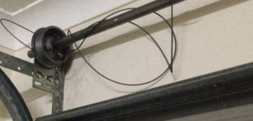 Garage door mechanism with a broken cable. The cable is wrapped around a rod and has come loose.