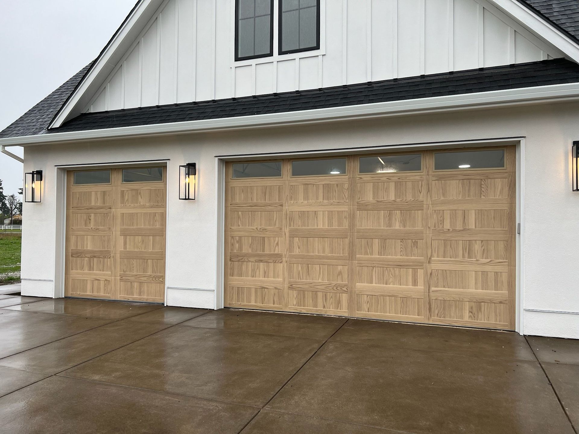 A white house with two wooden garage doors on a rainy day.