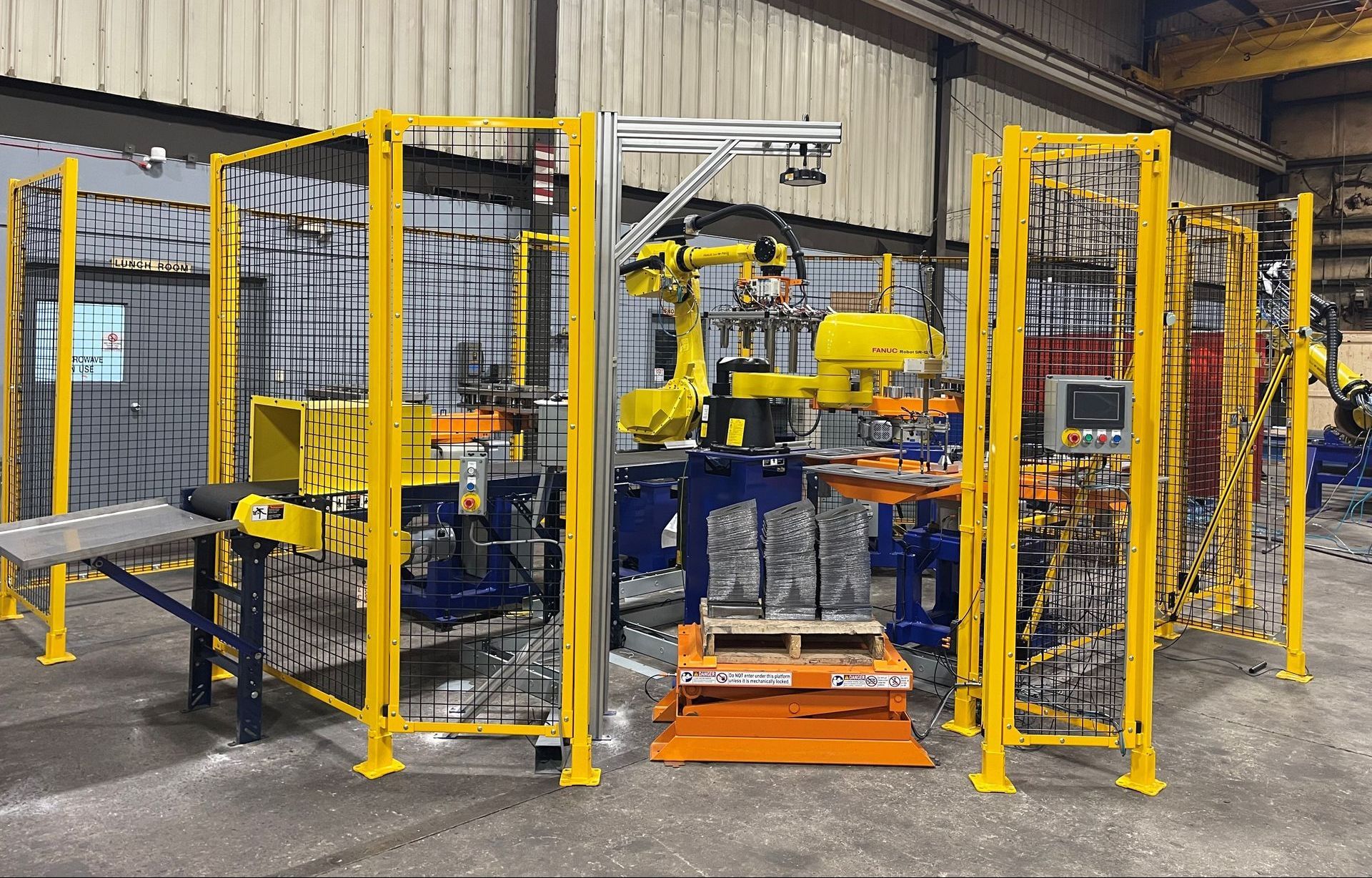 A robot is working on a machine in a factory behind a yellow fence.