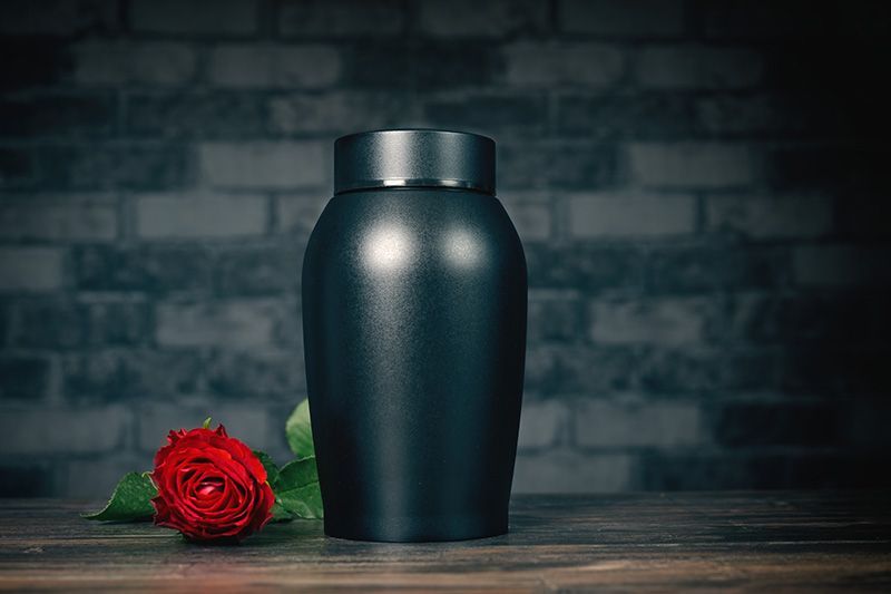 A black urn with a red rose on a wooden table.