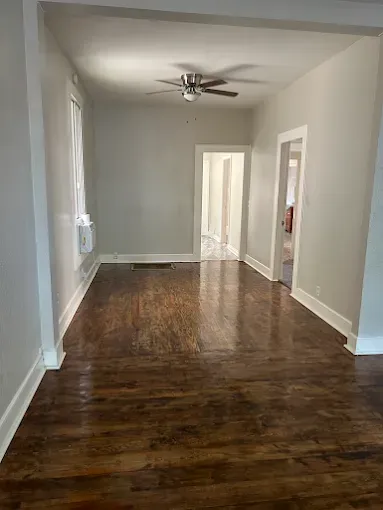 Empty living room with wood floors, light walls, and three doorways.