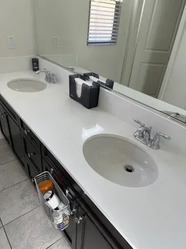 Bathroom with dual sinks, white countertop, dark cabinets, mirror, and window.