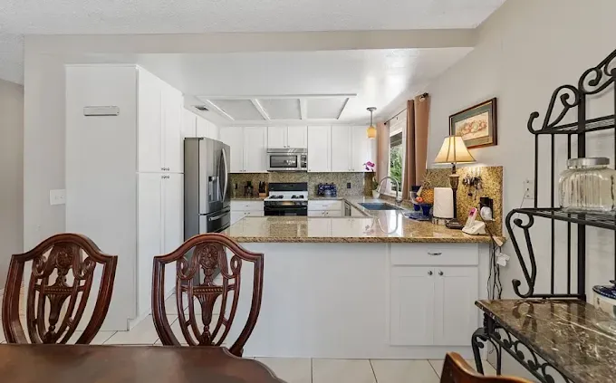 Kitchen with white cabinets, granite countertops, and ornate chairs.