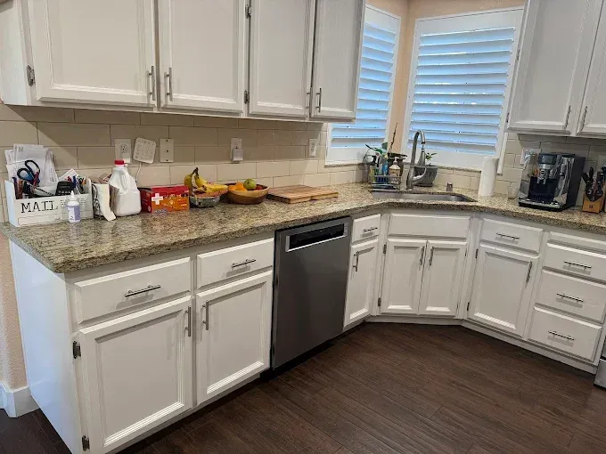 White kitchen with granite countertops, a stainless steel dishwasher, and dark wood floors.