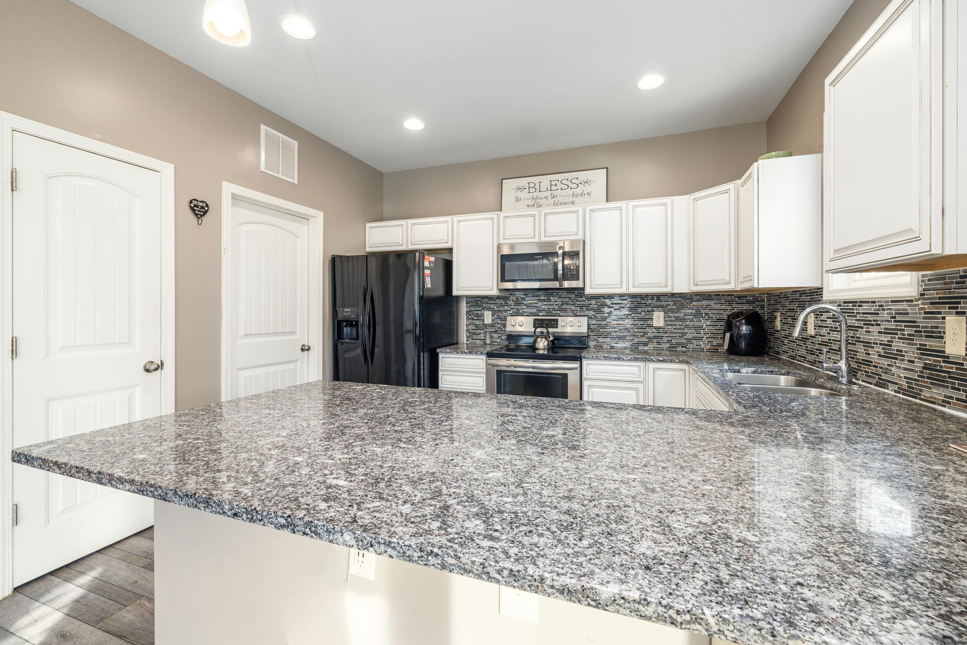 A modern kitchen with white cabinets, granite countertops, and black appliances.