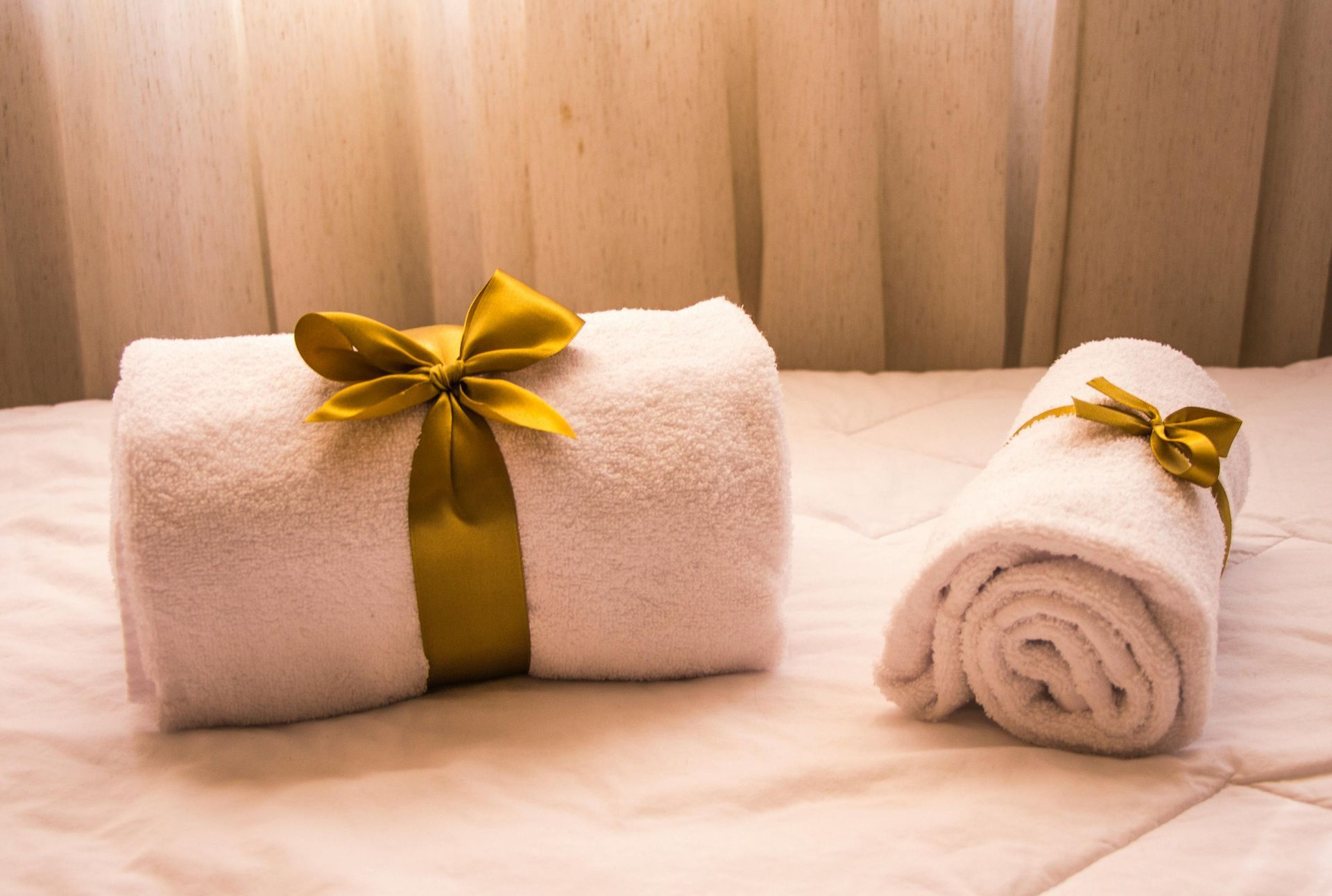 White towels rolled and tied with gold ribbons on a white bed.