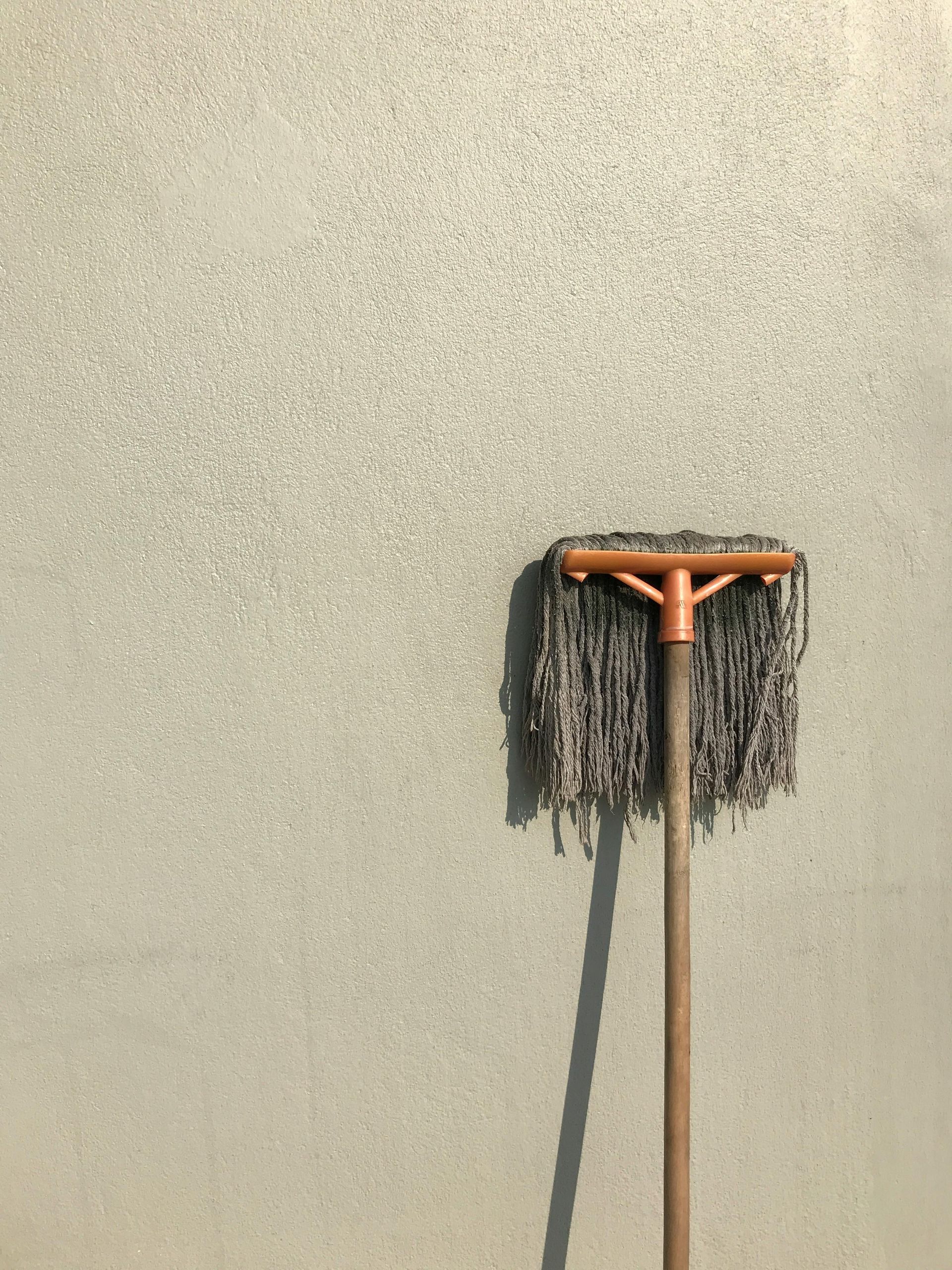 Mop leaning against a textured light gray wall, casting a shadow.