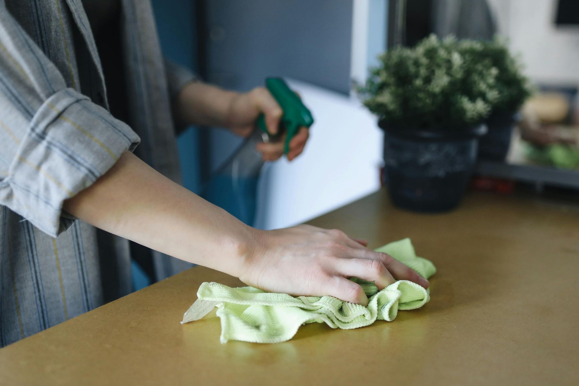 Person cleaning a wooden surface with a green cloth and spray bottle.
