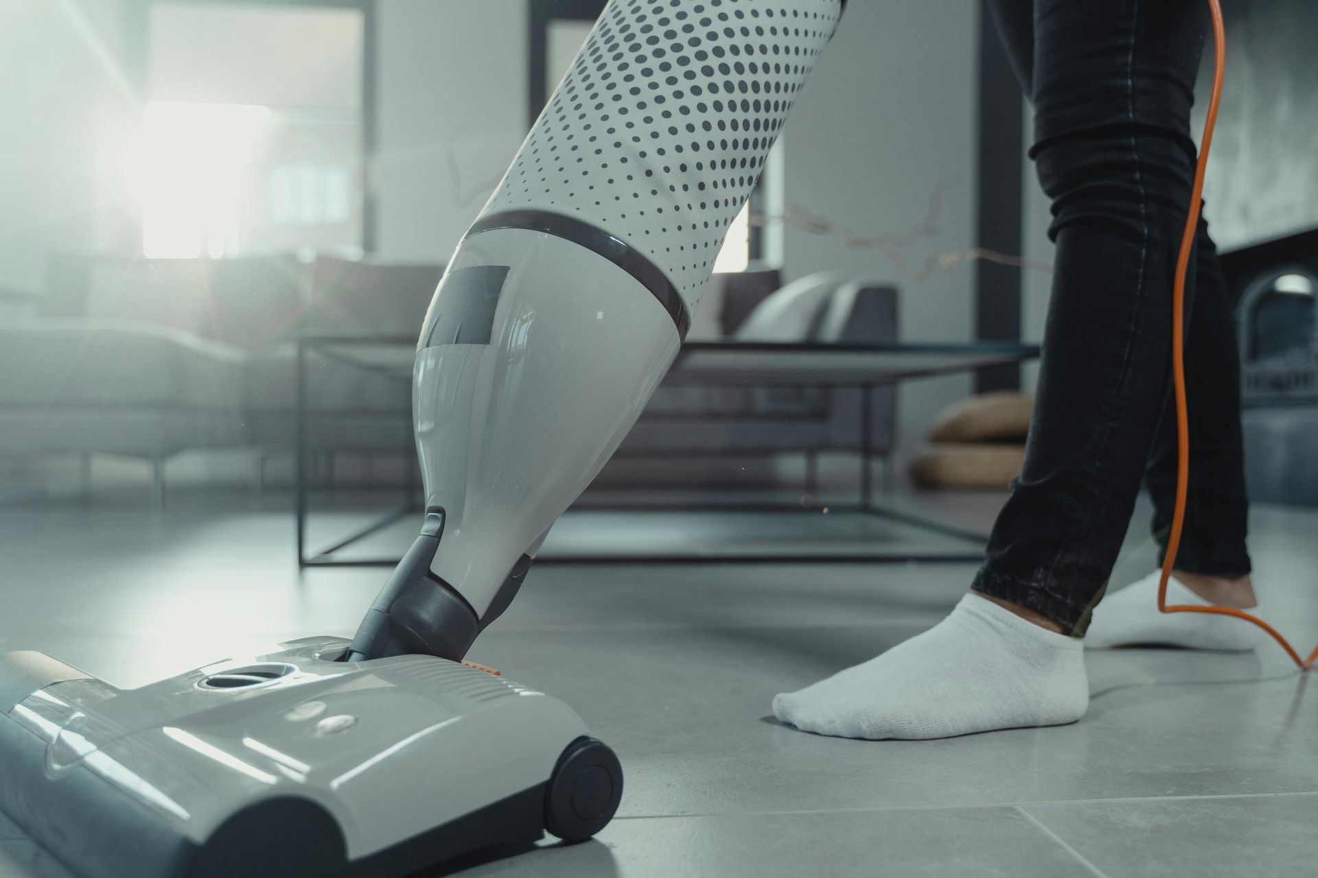 Person vacuuming a tiled floor with a white and gray vacuum cleaner in a living room.