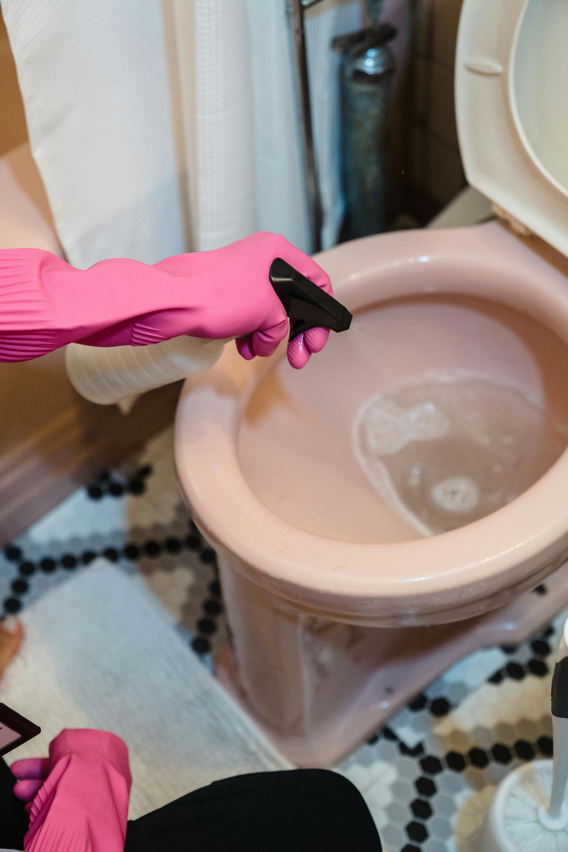 Person wearing pink gloves spraying cleaner into a pink toilet.