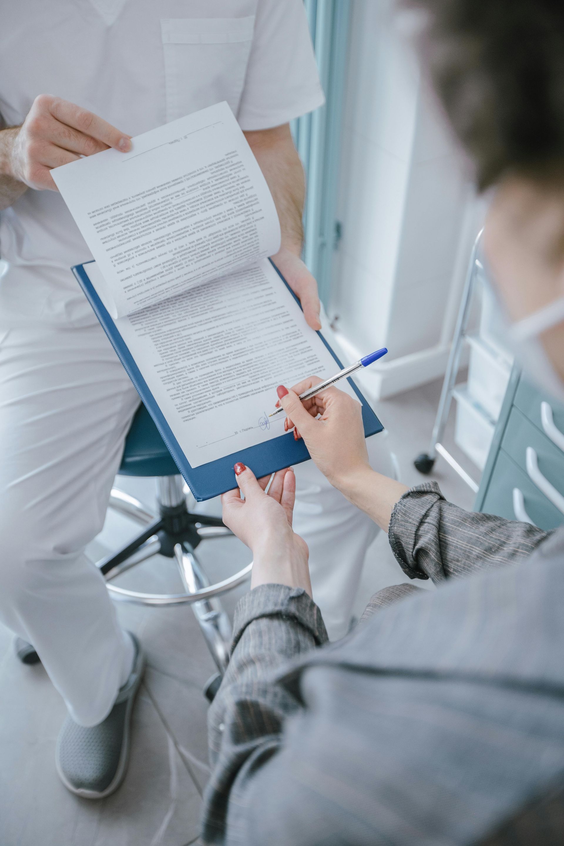 A dentist is talking to a patient who is writing on a clipboard.