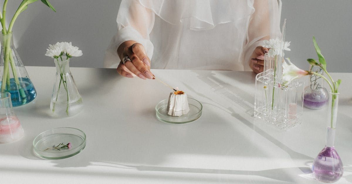 A woman is sitting at a table with flowers and beakers.