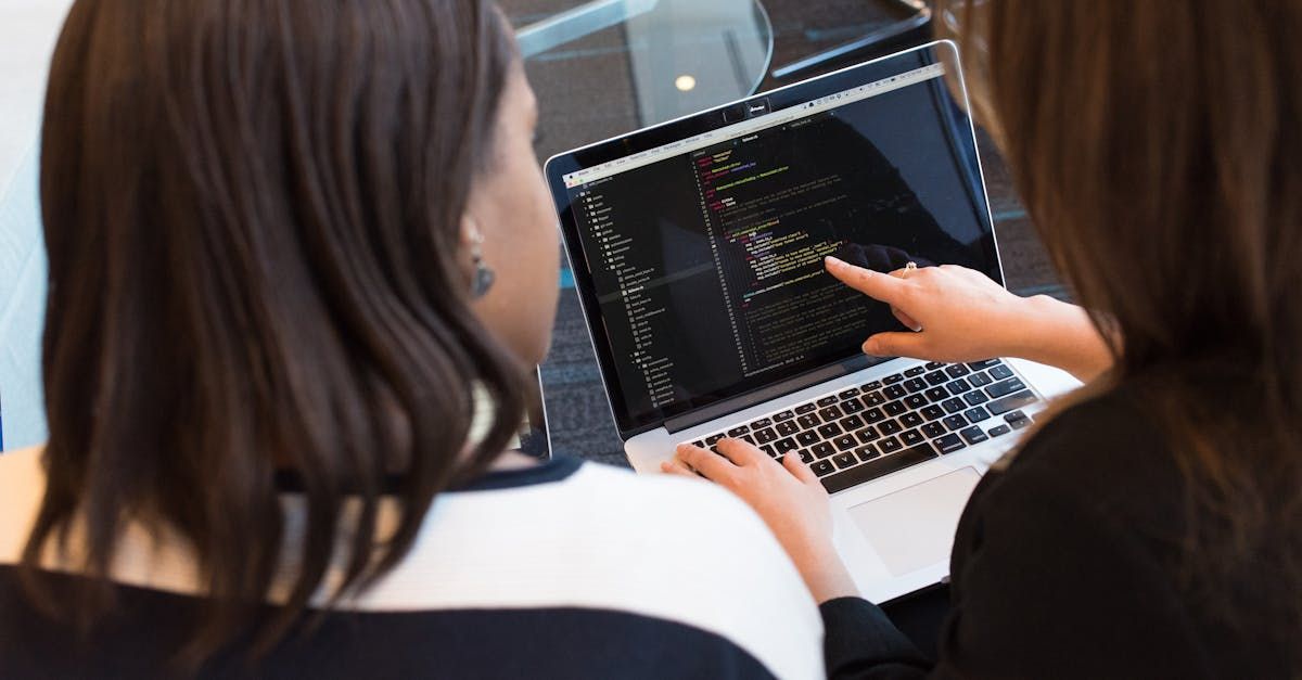 Two women are sitting in front of a laptop computer.