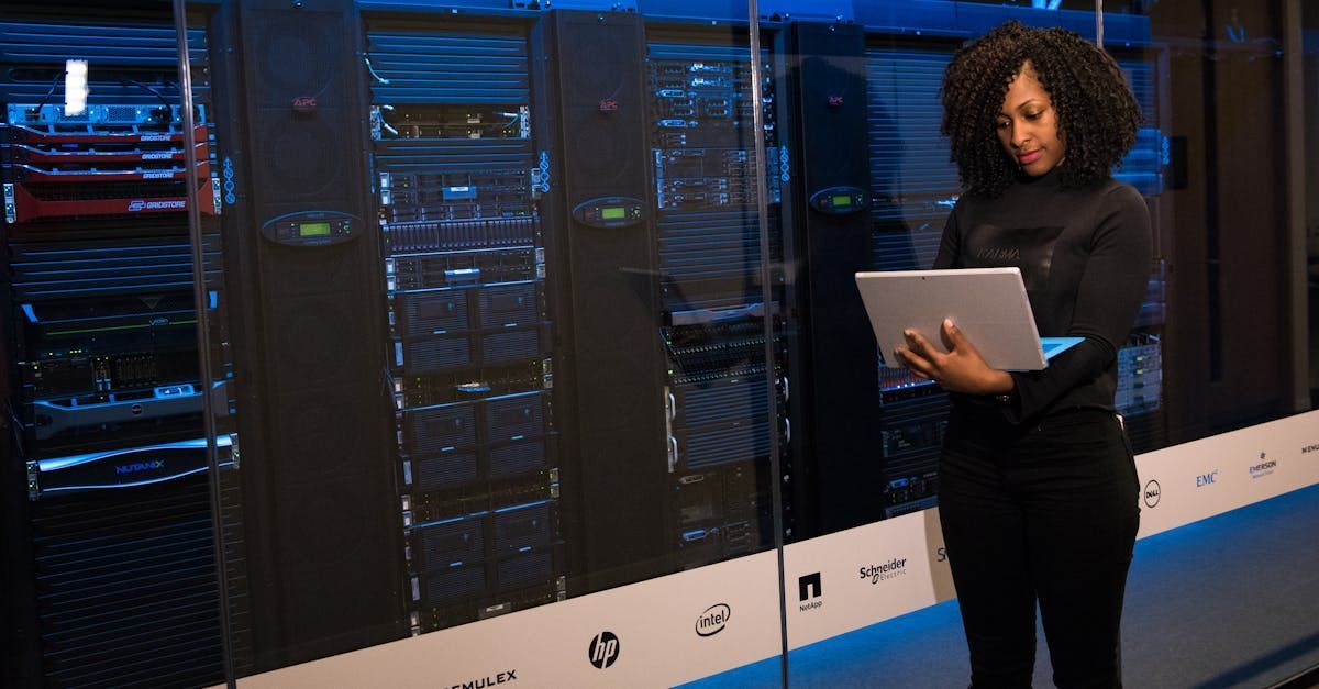 A woman is standing in a server room holding a laptop.