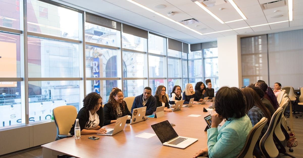 A group of people are sitting around a long table with laptops in a conference room.