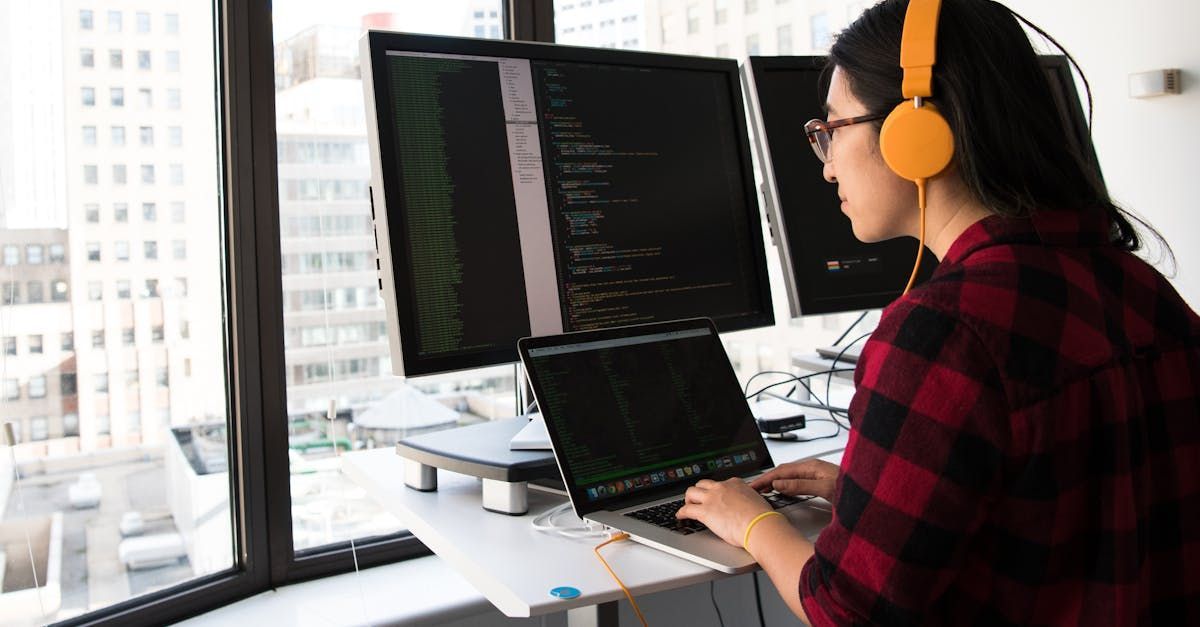 A woman wearing headphones is sitting at a desk using a laptop computer.