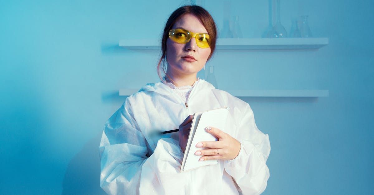 A woman in a lab coat and yellow glasses is holding a notebook.