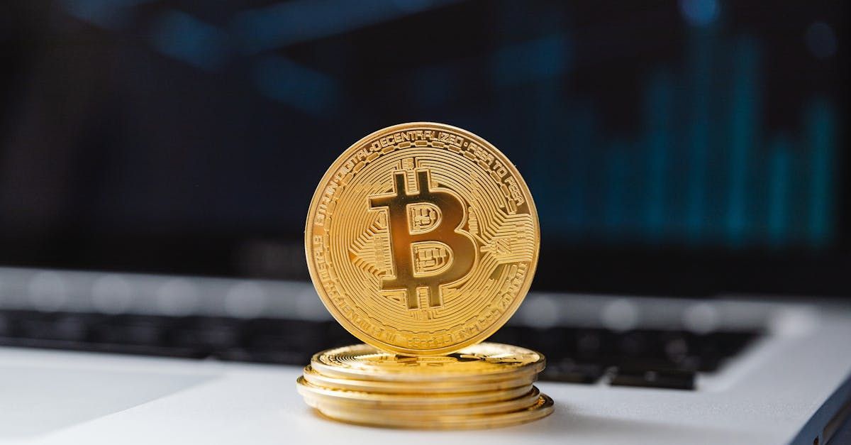 A gold bitcoin is sitting on top of a stack of gold coins on a laptop.