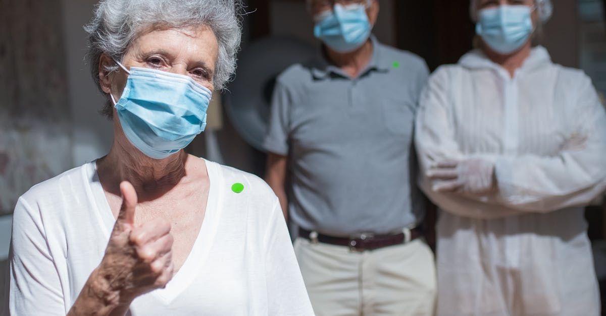 An elderly woman wearing a face mask is giving a thumbs up.