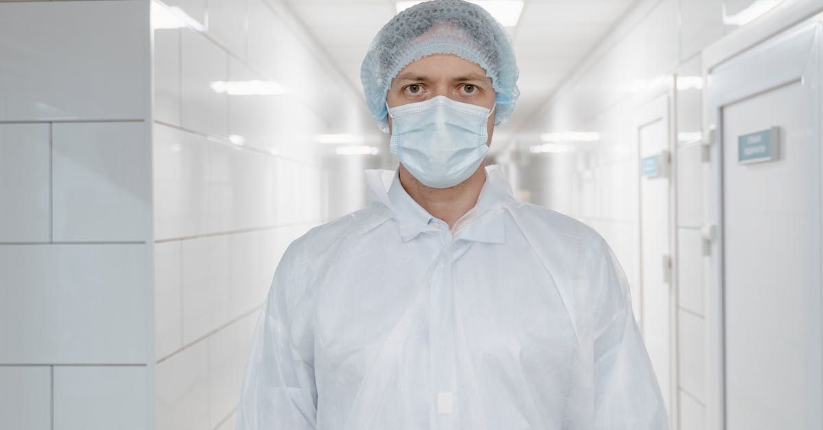 A surgeon wearing a mask and a cap is standing in a hospital hallway.