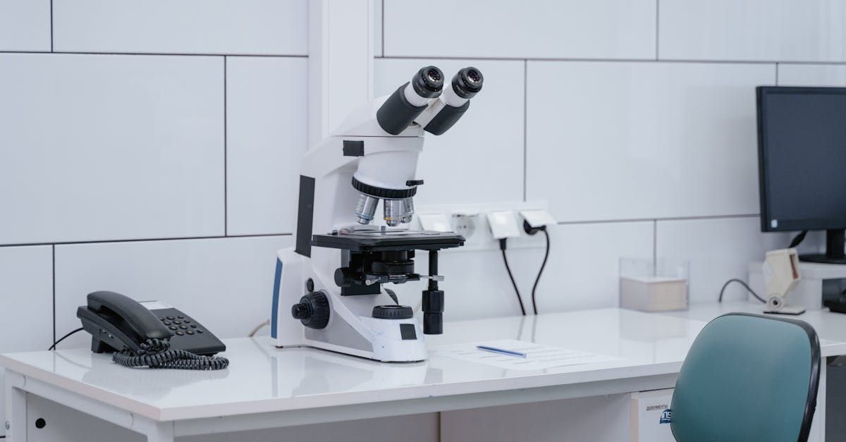 A microscope is sitting on top of a white desk in a lab.