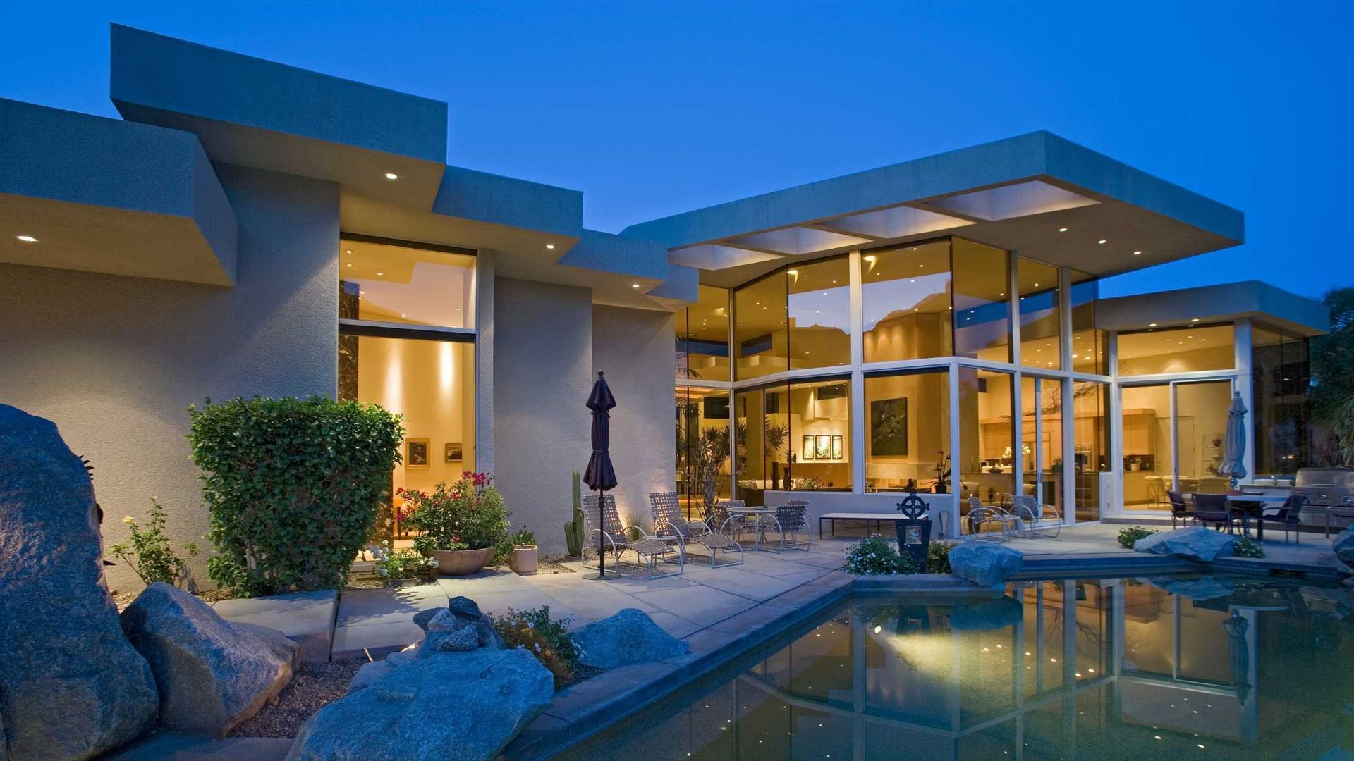 Modern home at dusk with pool, large windows, and outdoor seating.
