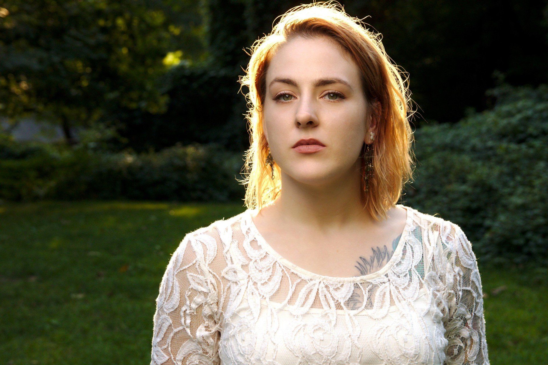 A woman in a white lace top is standing in the grass