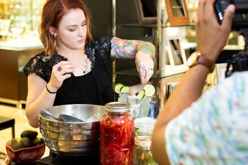 A woman is preparing food in a kitchen while a man takes a picture of her.
