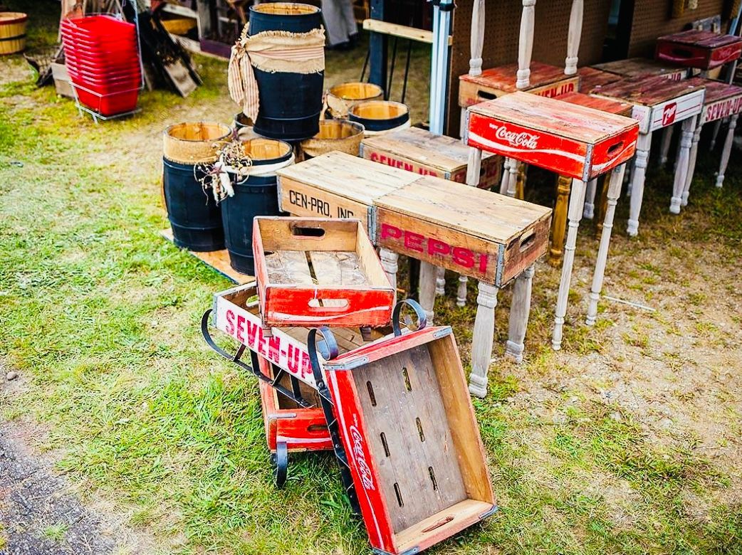 Vintage wooden crates, barrels, and tables outdoors on grass, various red and brown hues.