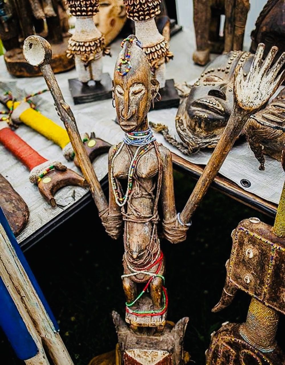 Wooden carved figure with outstretched arms holding tools, surrounded by other carvings.