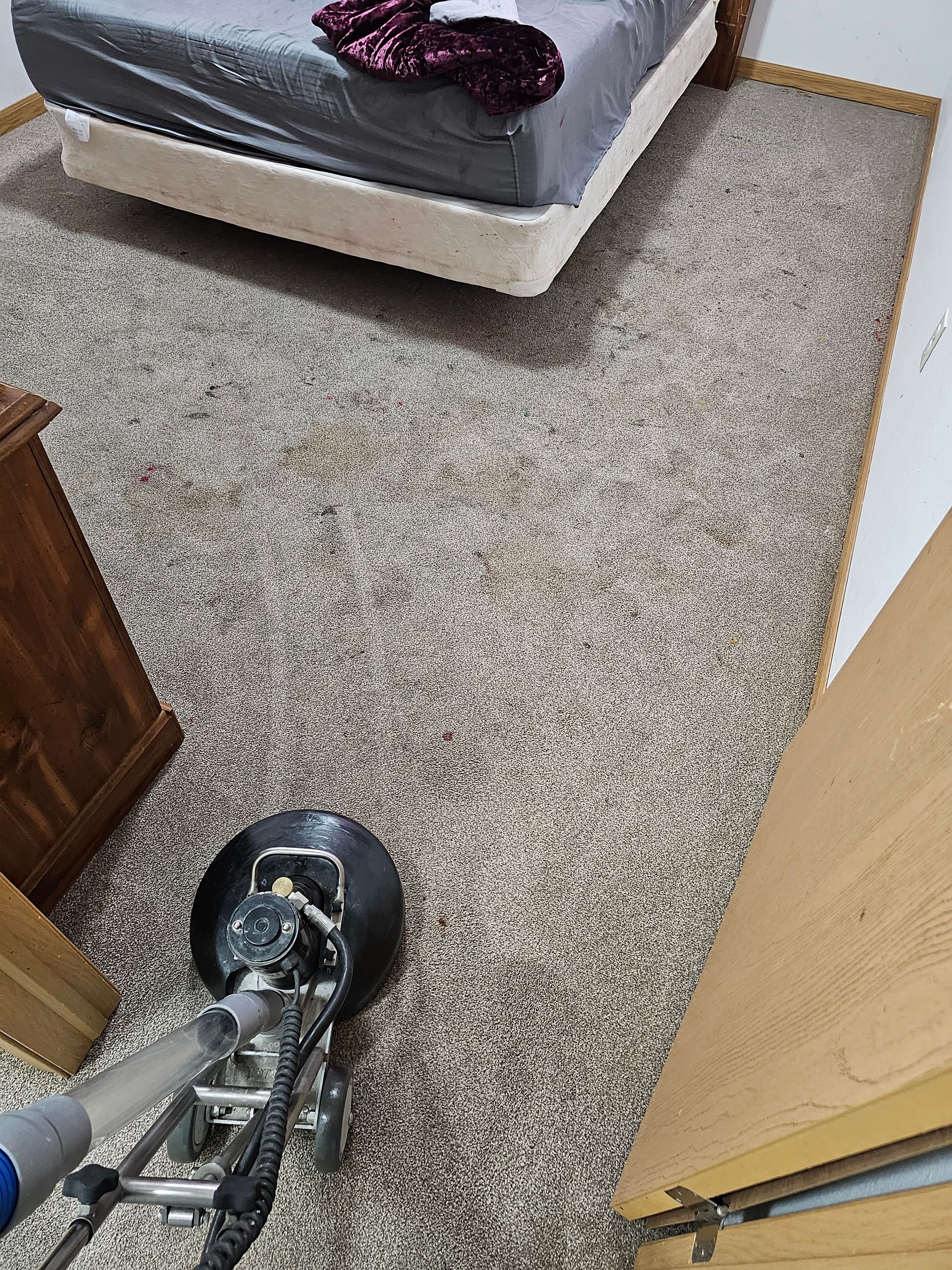 A vacuum cleaner is being used to clean a carpet in a bedroom.