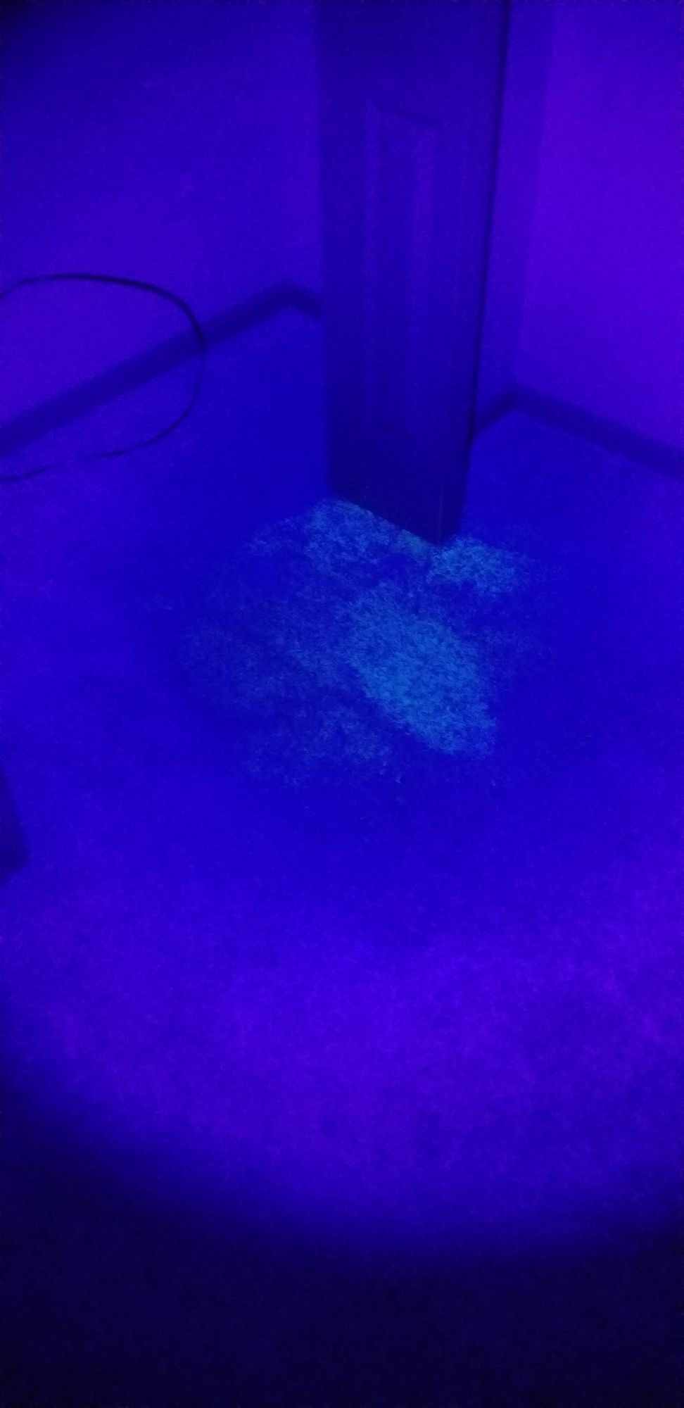 A blue light is shining on a couch in a dark room.