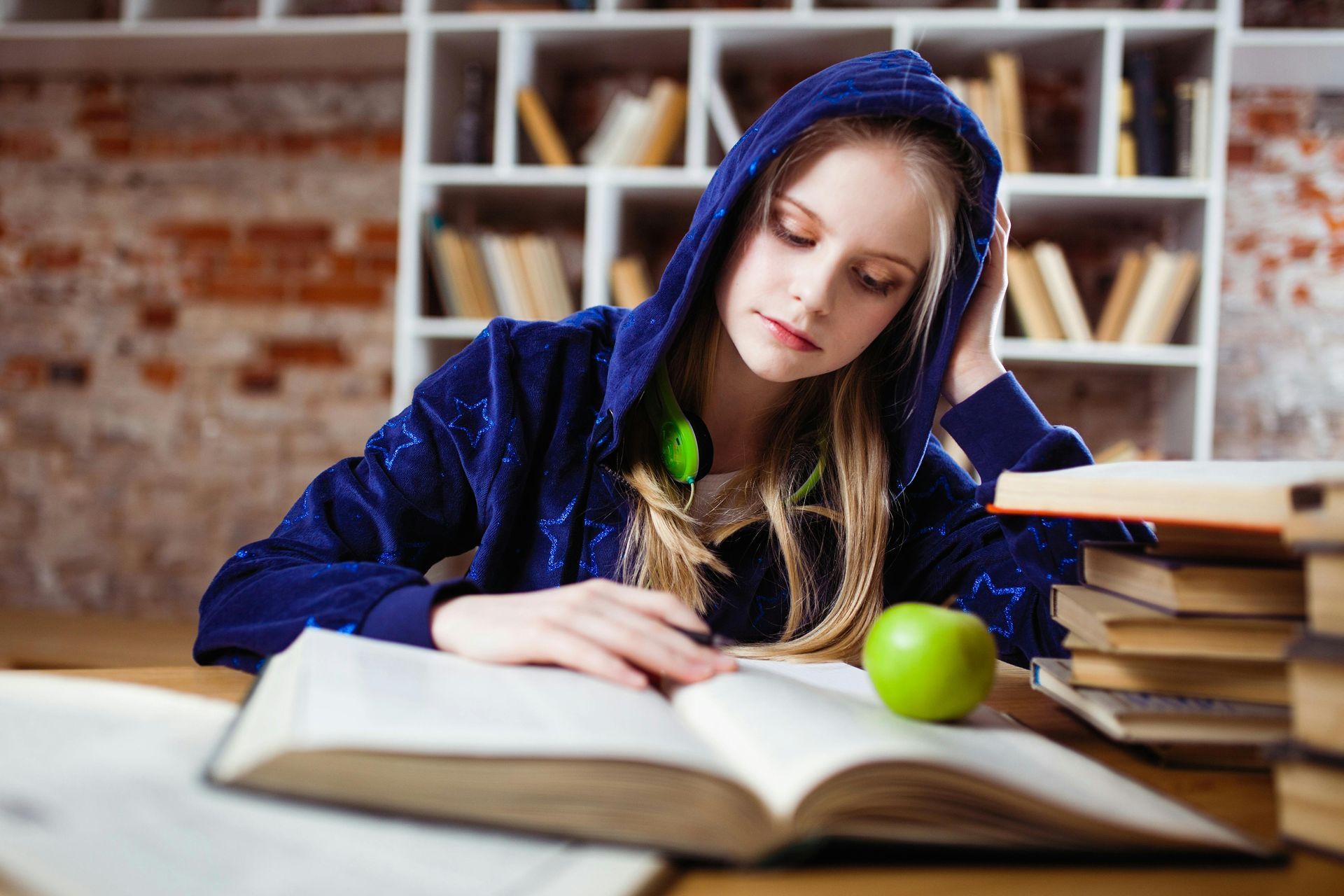 A girl in a hoodie is reading a book in a library.