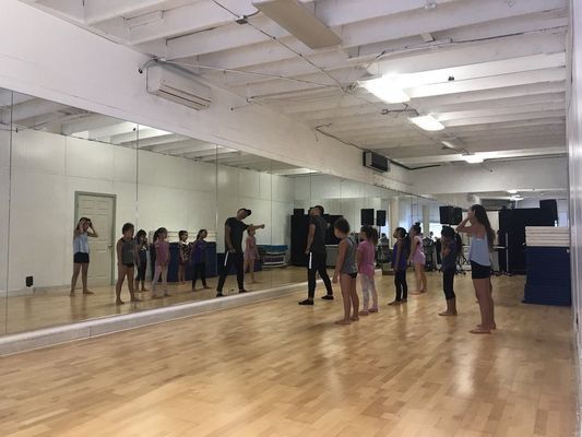 A group of children are standing in front of a large mirror in a dance studio.