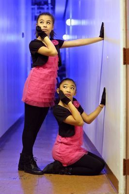 Two girls are kneeling down in a hallway and one is leaning against a wall